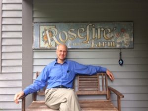 Man sitting on a bench underneath a sign that reads "Rosefire Farm."
