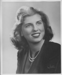 A 1940's black and white studio portrait of my mom with white teeth, dark lipstick and a double strant of pears over her suit jacket.