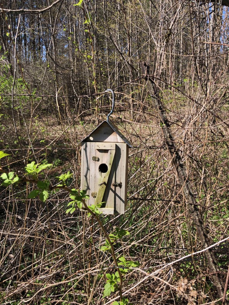 A birdhouse hanging on a fence wire