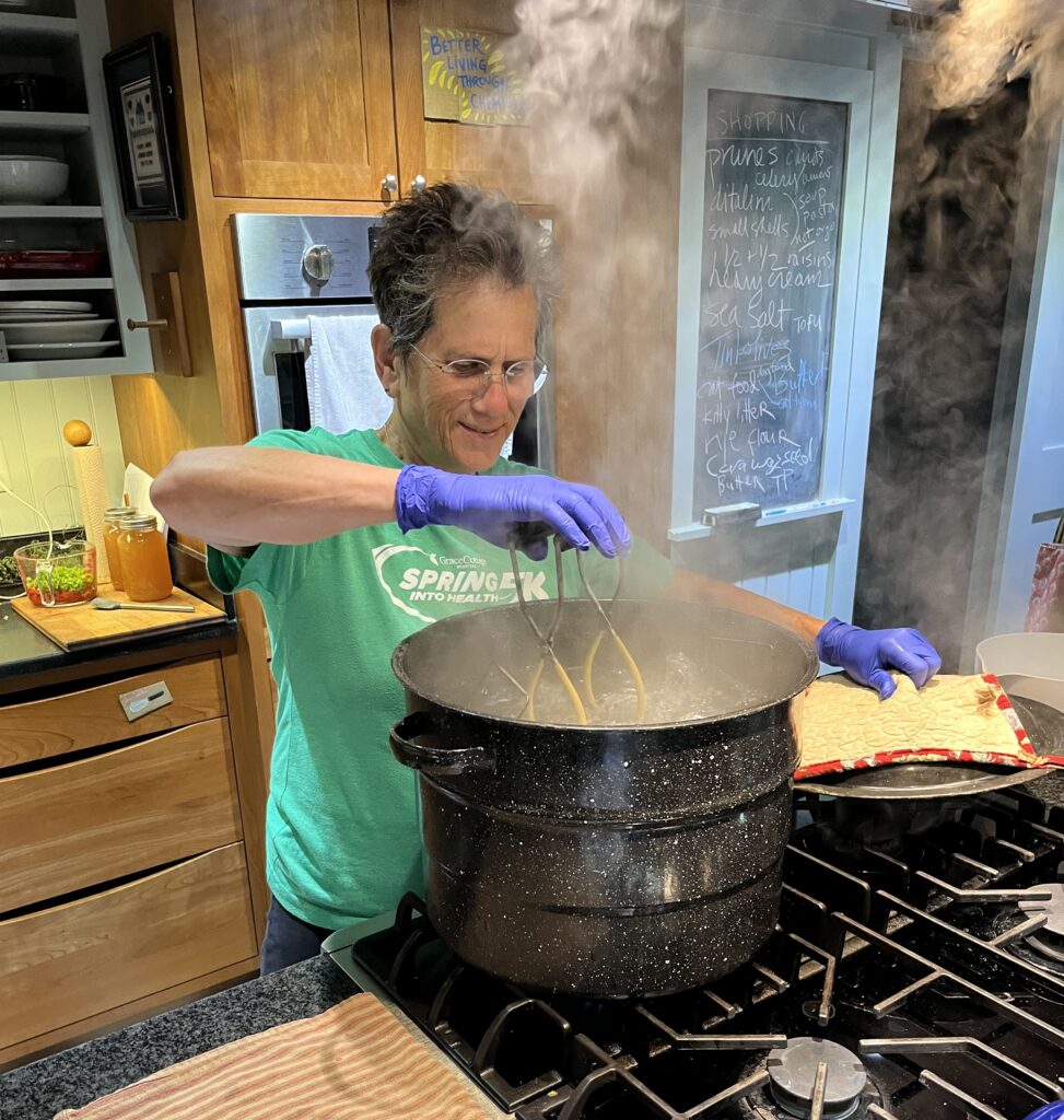 Woman wearing green t-shirt standing at stove looking into a steaming black kettle.